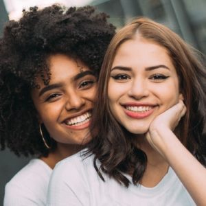 two-women-smiling-hugging-manifesting-love-wearing-white-shirt Two women smiling, hugging and manifesting love, wearing white t-shirts.